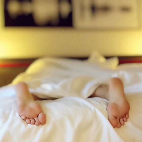Photo by Pixabay A person relaxing on a bed with feet under white sheets, conveying serenity